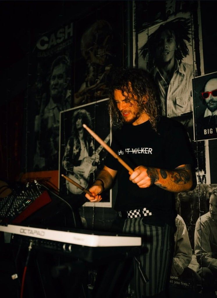A drummer mid-set on the Filthy's stage in front of the venue's poster wall