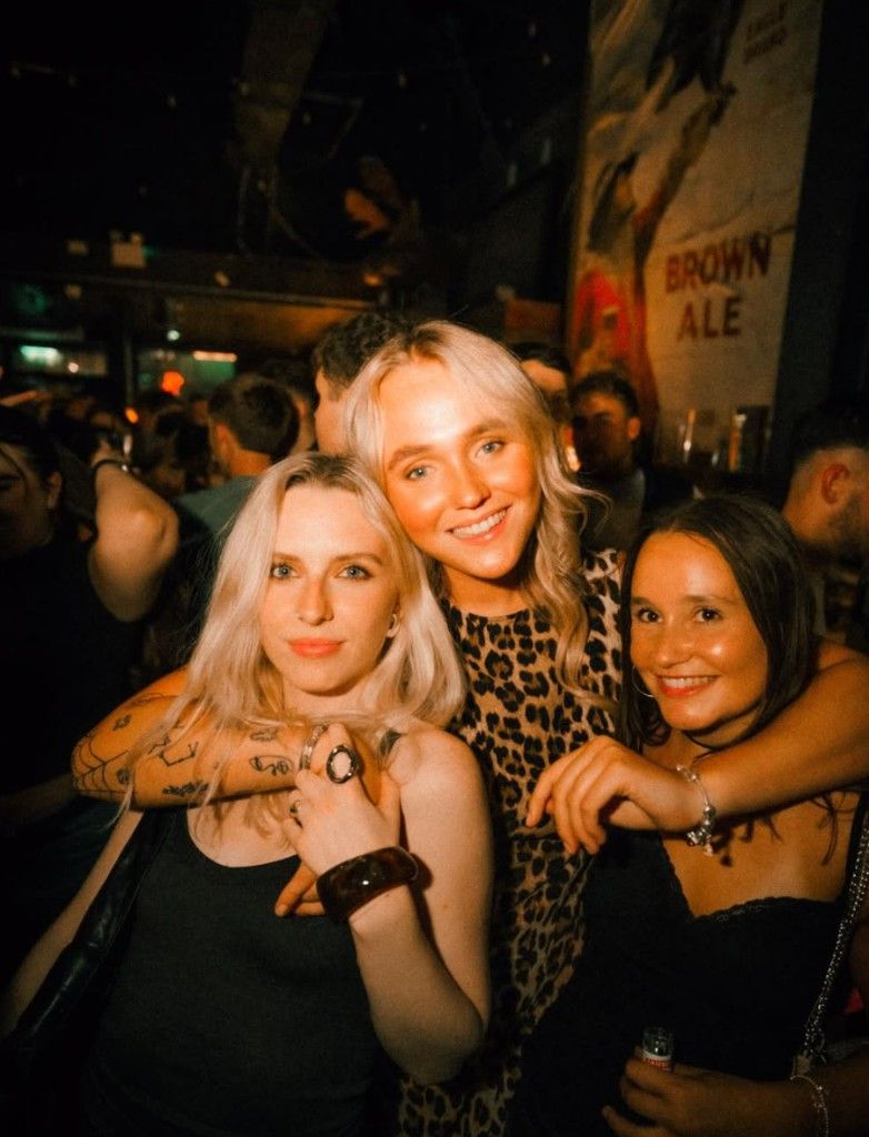 Three friends smiling together at the bar in Filthy's